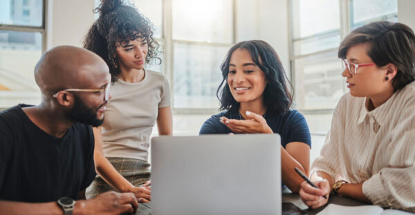 Laptop, digital marketing and team in a meeting planning seo, advertising and innovation strategy as a group. Creative, diversity and young people working on branding ideas for a startup project